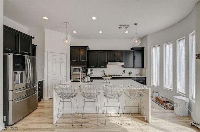 kitchen featuring stainless steel appliances, a breakfast bar, an island with sink, and hanging light fixtures