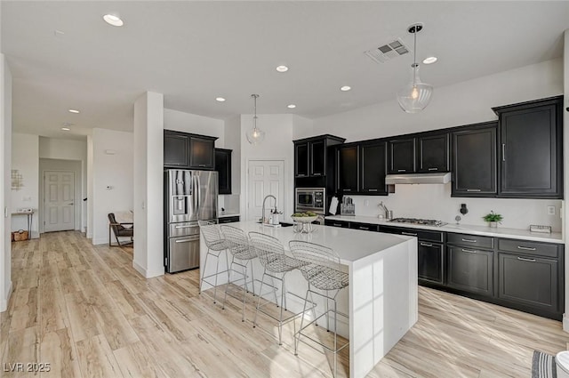 kitchen featuring appliances with stainless steel finishes, a kitchen island with sink, a kitchen breakfast bar, light hardwood / wood-style floors, and decorative light fixtures