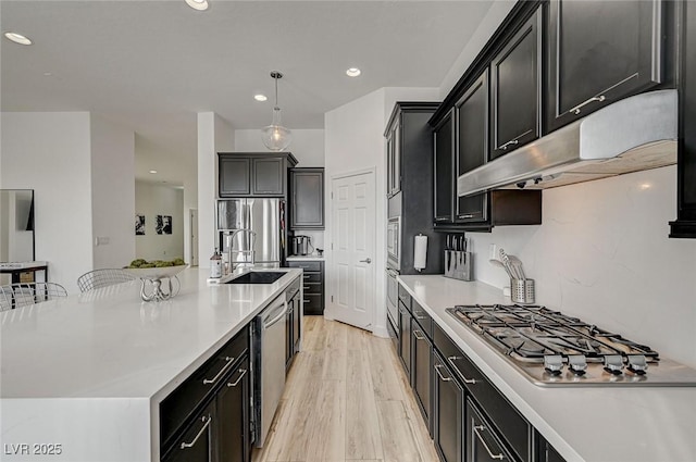 kitchen with sink, light hardwood / wood-style flooring, appliances with stainless steel finishes, decorative light fixtures, and a large island with sink