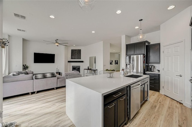 kitchen with appliances with stainless steel finishes, an island with sink, sink, ceiling fan, and light hardwood / wood-style floors