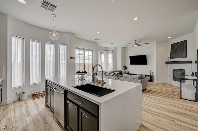 kitchen with sink, dishwasher, hanging light fixtures, light hardwood / wood-style floors, and an island with sink