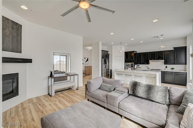 living room with a tiled fireplace, ceiling fan, and light hardwood / wood-style flooring