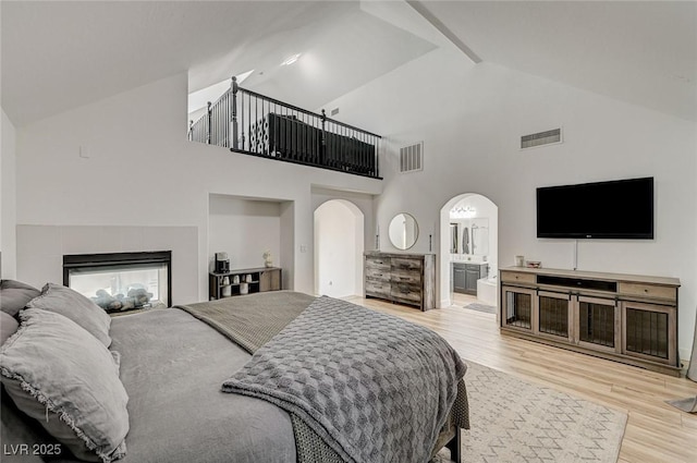 bedroom featuring ensuite bathroom, high vaulted ceiling, light wood-type flooring, and a fireplace