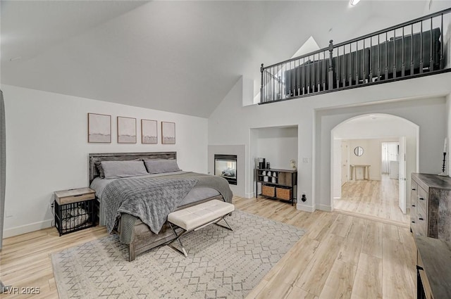 bedroom with a towering ceiling, connected bathroom, a multi sided fireplace, and light wood-type flooring