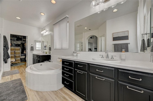 bathroom featuring hardwood / wood-style flooring, vanity, and a relaxing tiled tub