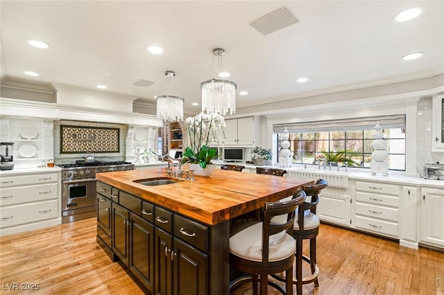 kitchen with wood counters, high end range, a kitchen island with sink, decorative backsplash, and white cabinets