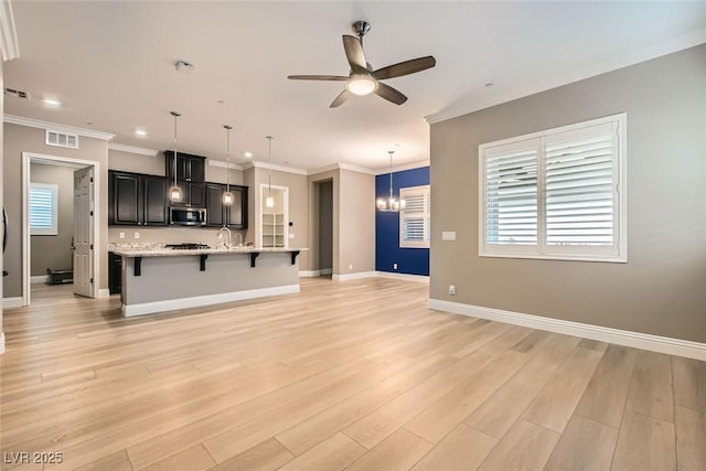 kitchen featuring ceiling fan with notable chandelier, a kitchen breakfast bar, hanging light fixtures, a center island with sink, and light wood-type flooring