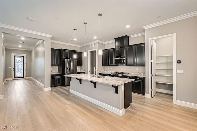 kitchen featuring a breakfast bar area, light wood-type flooring, pendant lighting, stainless steel appliances, and a kitchen island with sink