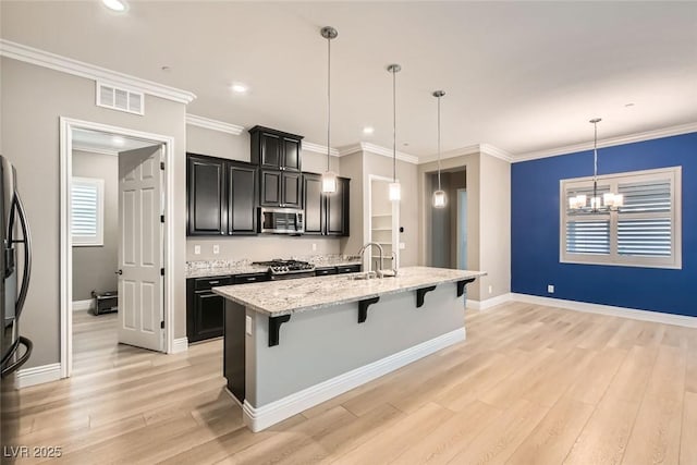 kitchen featuring pendant lighting, a kitchen bar, stainless steel appliances, light stone countertops, and a center island with sink