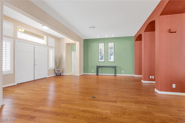 foyer featuring light wood-style flooring, arched walkways, and baseboards