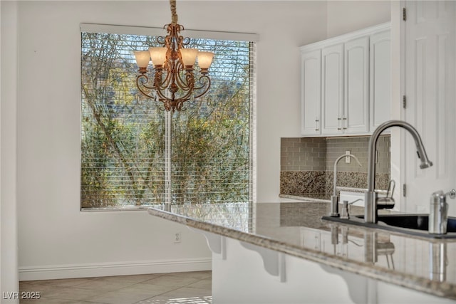 kitchen with white cabinetry, tasteful backsplash, a chandelier, light tile patterned floors, and light stone countertops