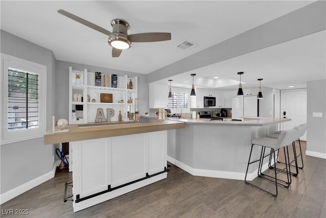 kitchen featuring stainless steel range with electric cooktop, white cabinetry, decorative light fixtures, a kitchen breakfast bar, and kitchen peninsula