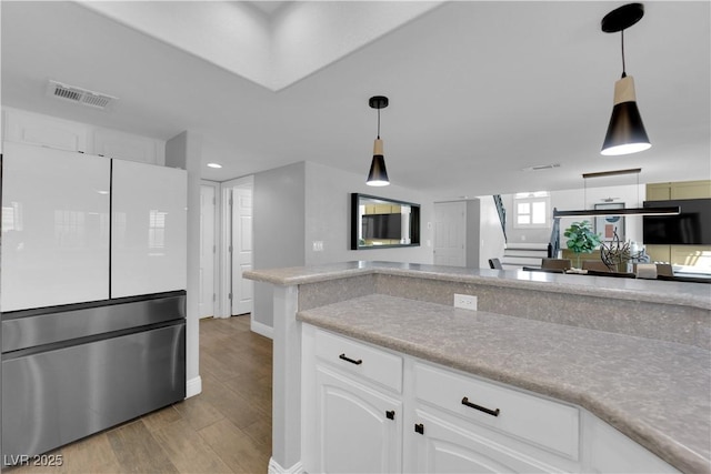 kitchen with white cabinetry, decorative light fixtures, white fridge, and light wood-type flooring