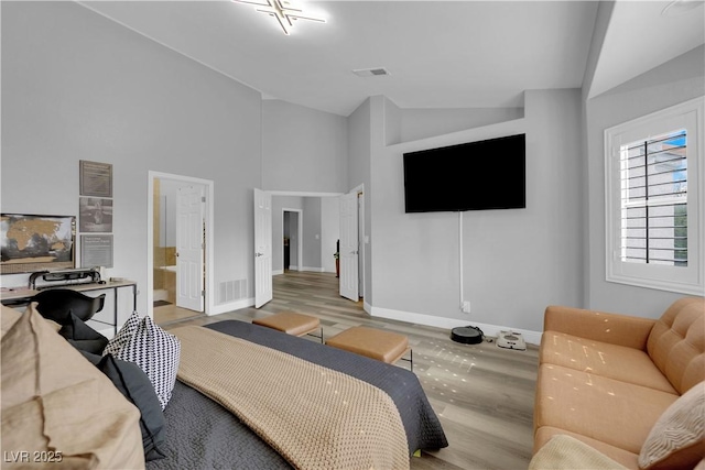 bedroom with high vaulted ceiling, light wood-type flooring, and ensuite bath