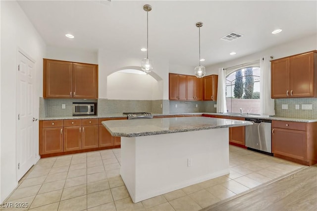 kitchen featuring appliances with stainless steel finishes, a center island, light stone counters, light tile patterned flooring, and decorative light fixtures