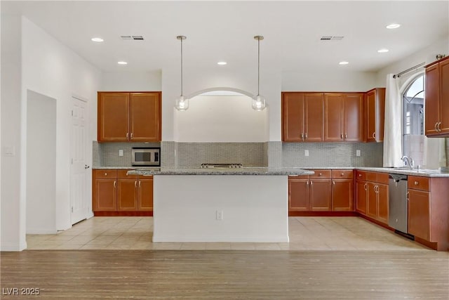 kitchen with hanging light fixtures, backsplash, stainless steel appliances, a center island, and light stone countertops