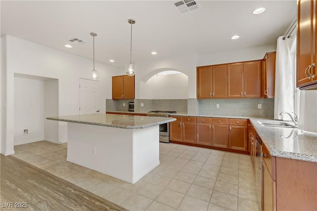 kitchen featuring sink, light stone counters, a kitchen island, decorative light fixtures, and stainless steel range with gas cooktop