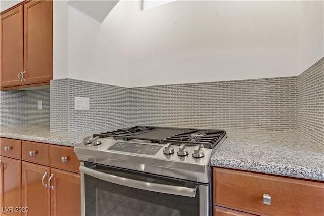 kitchen featuring stainless steel gas stove, light stone countertops, tasteful backsplash, and tile patterned floors