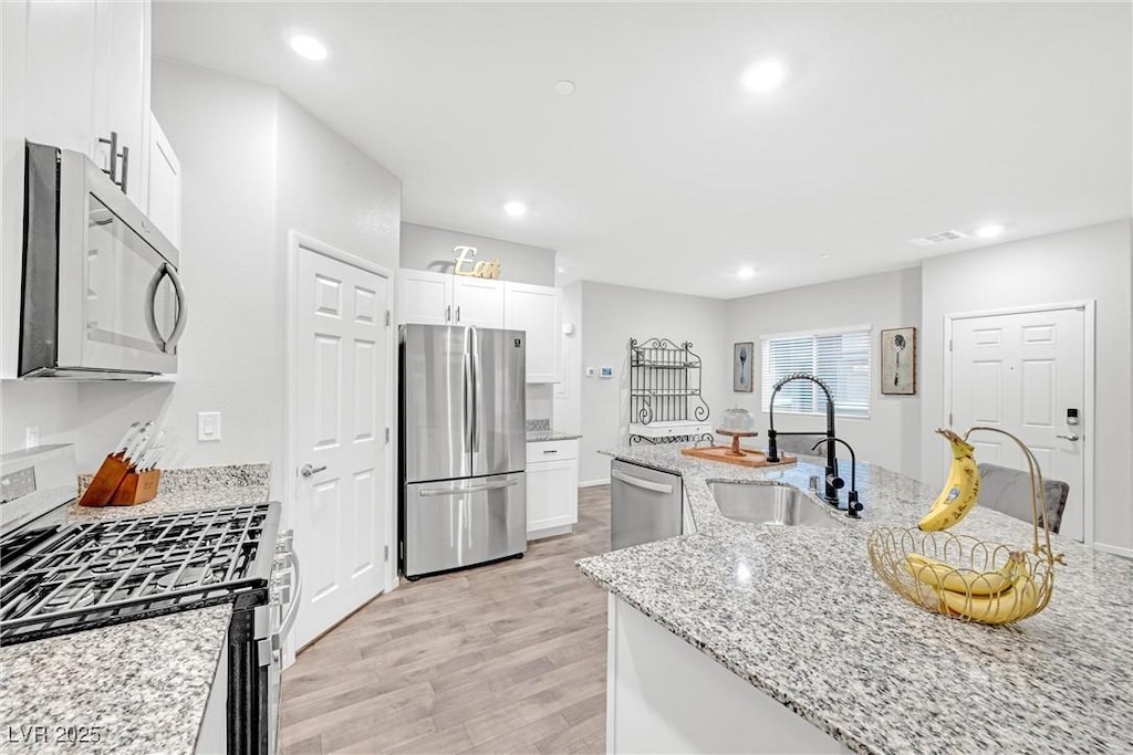 kitchen featuring appliances with stainless steel finishes, sink, white cabinets, light stone countertops, and light hardwood / wood-style flooring