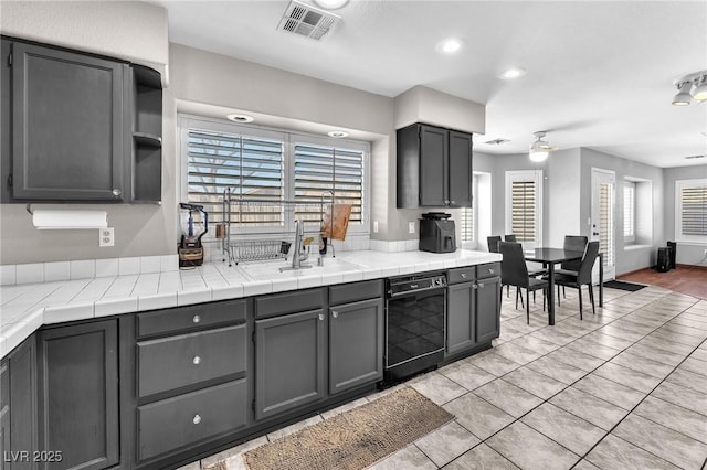 kitchen featuring ceiling fan, light tile patterned floors, tile countertops, and black dishwasher