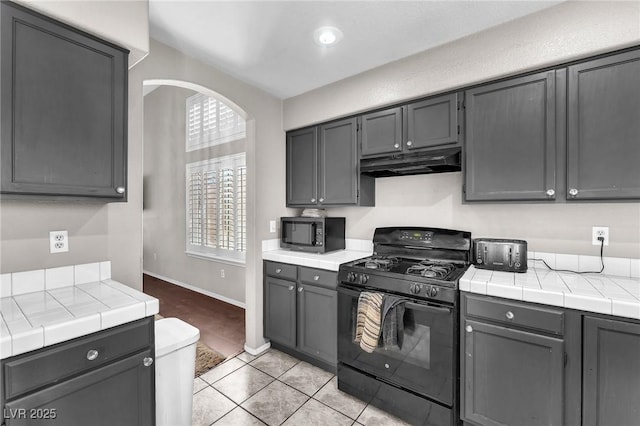 kitchen featuring gray cabinetry, tile counters, light tile patterned flooring, and black appliances