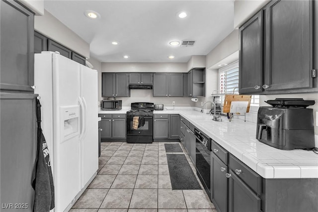 kitchen featuring sink, gray cabinetry, tile countertops, light tile patterned floors, and black appliances