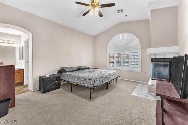 bedroom with lofted ceiling, a tiled fireplace, ensuite bath, and light colored carpet