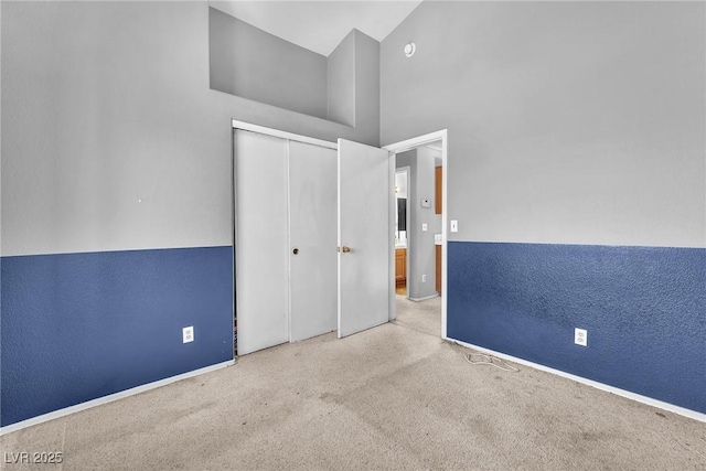 unfurnished bedroom with light colored carpet, high vaulted ceiling, and a closet