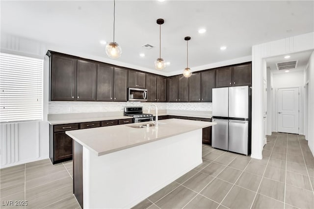 kitchen featuring decorative light fixtures, sink, a kitchen island with sink, dark brown cabinetry, and stainless steel appliances