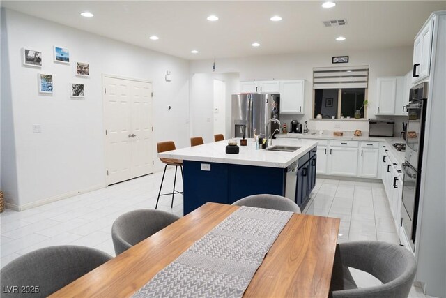 kitchen with stainless steel appliances, white cabinetry, a kitchen island with sink, and a kitchen breakfast bar