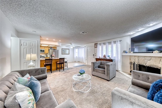 carpeted living room featuring ceiling fan, a fireplace, and a textured ceiling