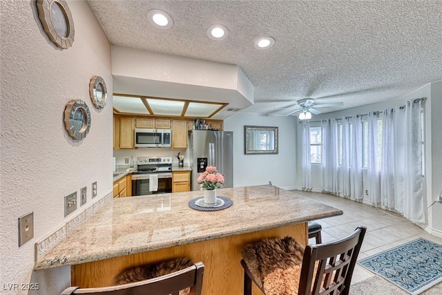 kitchen featuring light tile patterned floors, a breakfast bar area, appliances with stainless steel finishes, a textured ceiling, and kitchen peninsula