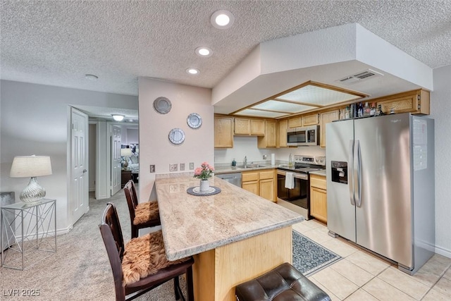 kitchen with sink, a kitchen breakfast bar, stainless steel appliances, light brown cabinetry, and kitchen peninsula