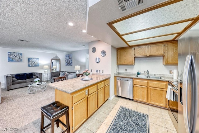 kitchen with sink, a breakfast bar area, a textured ceiling, kitchen peninsula, and stainless steel appliances