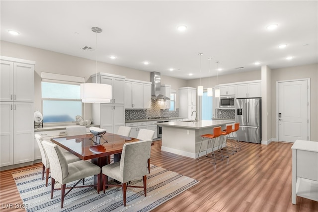 kitchen featuring an island with sink, backsplash, hanging light fixtures, high end appliances, and wall chimney exhaust hood