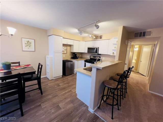 kitchen with a breakfast bar area, visible vents, a peninsula, white cabinets, and appliances with stainless steel finishes