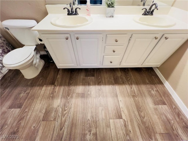 bathroom featuring double vanity, toilet, wood finished floors, and a sink