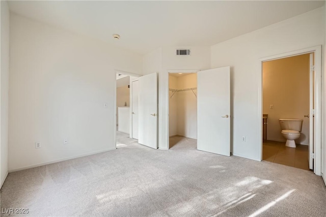 unfurnished bedroom with light carpet, a spacious closet, ensuite bath, and a closet