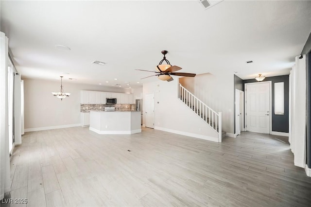 unfurnished living room featuring ceiling fan with notable chandelier and light wood-type flooring