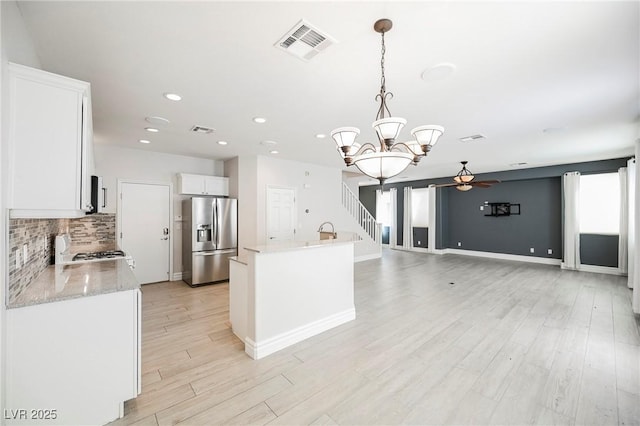 kitchen with white cabinetry, range, stainless steel fridge with ice dispenser, an island with sink, and pendant lighting