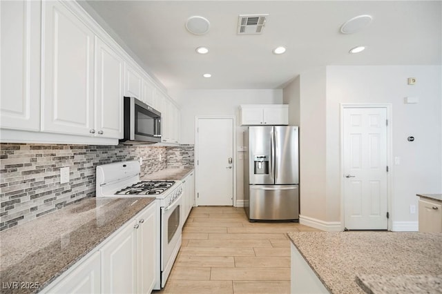 kitchen featuring appliances with stainless steel finishes, light stone counters, light hardwood / wood-style floors, white cabinets, and decorative backsplash