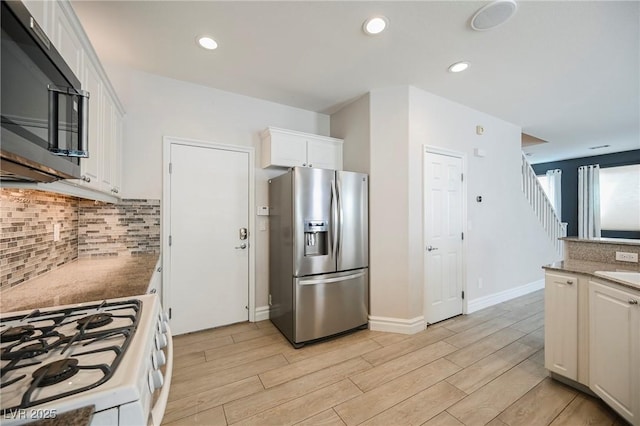 kitchen with stainless steel fridge with ice dispenser, white cabinetry, sink, decorative backsplash, and gas range gas stove