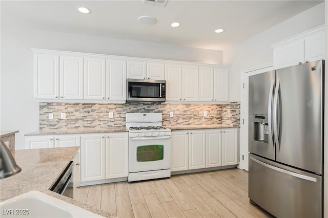 kitchen with stainless steel appliances, white cabinetry, light stone countertops, and decorative backsplash