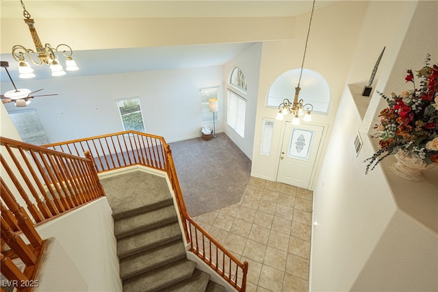 entrance foyer with a towering ceiling, carpet flooring, and ceiling fan with notable chandelier