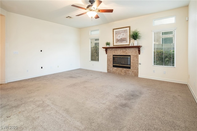 unfurnished living room with a tile fireplace, carpet floors, and ceiling fan