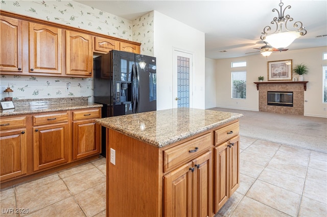 kitchen featuring a tile fireplace, light stone counters, a kitchen island, decorative light fixtures, and black fridge