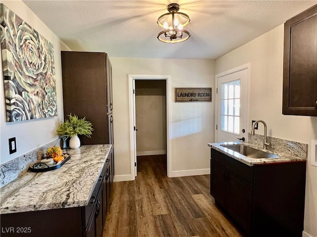 kitchen featuring light stone countertops, sink, dark brown cabinets, and a textured ceiling