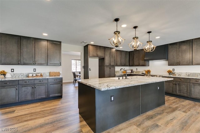 kitchen featuring a center island with sink, extractor fan, dark brown cabinets, and light wood-type flooring