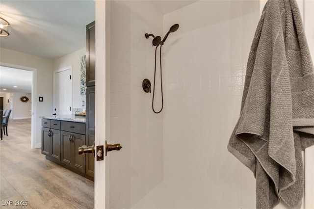 bathroom with wood-type flooring, a tile shower, and vanity