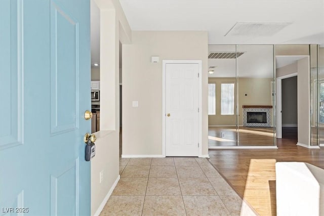 foyer entrance with light tile patterned floors, a glass covered fireplace, visible vents, and baseboards